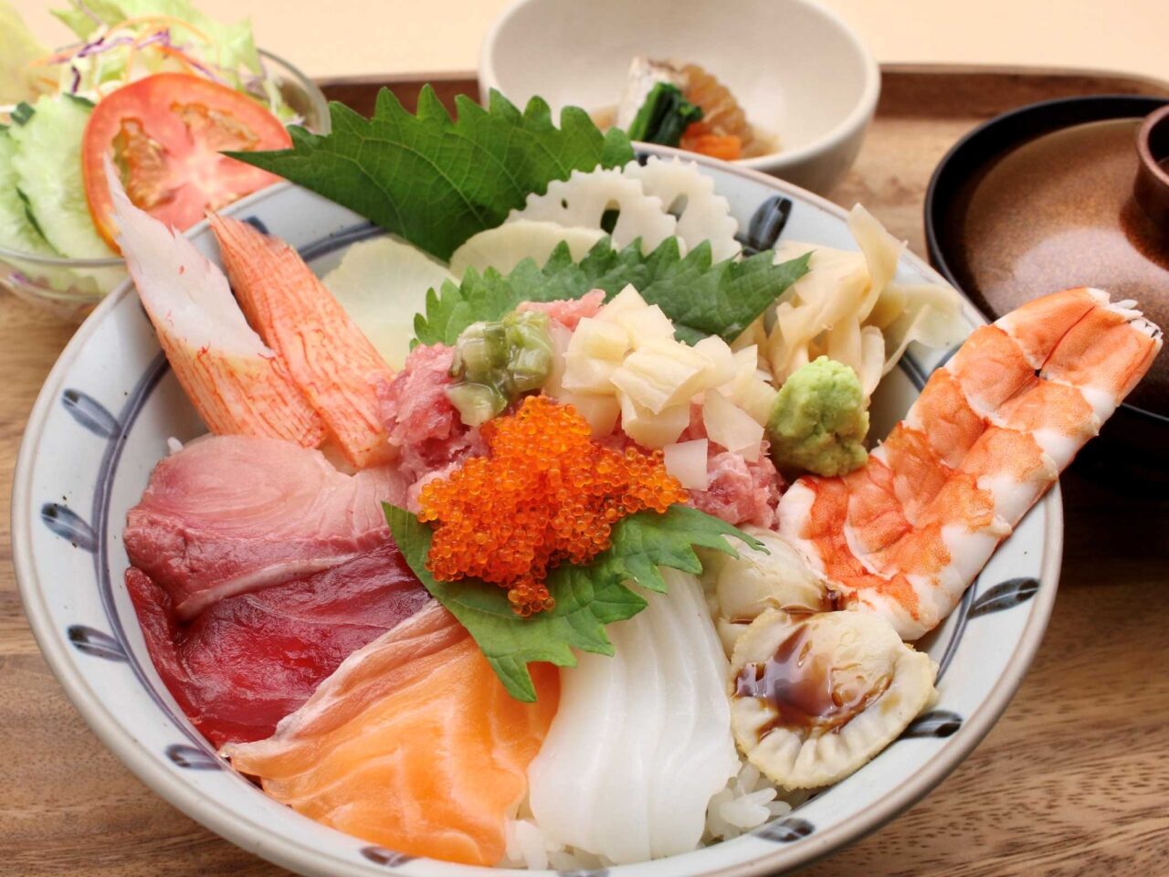 An abundant Japanese Kaisen Torotaku Don seafood rice bowl lunch set at Sushi Rin in Phrom Phong, Bangkok (490 THB). The ceramic bowl is richly topped with minced fatty tuna and crunchy pickled radish (Torotaku), vibrant flying fish roe (tobiko), fresh tuna, salmon, yellowtail, tender squid, glazed scallop, boiled shrimp, and crab stick over sushi rice, served on a wooden tray with a garden salad, Japanese side dish, and miso soup. Reference filename: sushi-rin-5.jpg.
