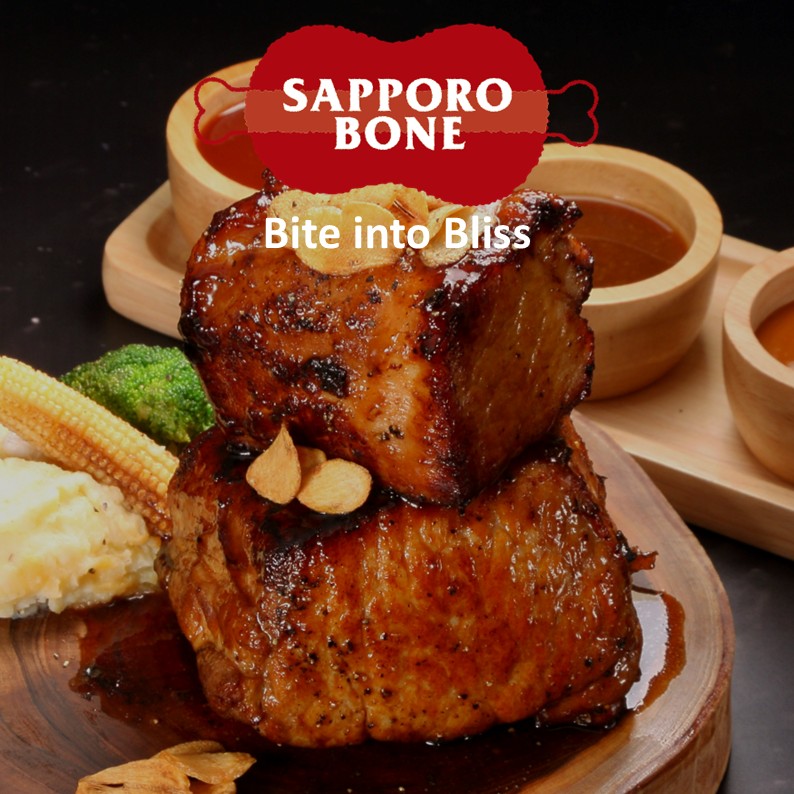 Thick-cut Japanese-style pork steak (Tonteki) stacked in two layers, topped with crispy garlic chips and rich savory sauce, served on a wooden plate with mashed potatoes, baby corn, and broccoli at SAPPORO BONE on the 6th floor of CentralWorld, Bangkok. The image features the SAPPORO BONE logo and the tagline "Bite into Bliss". File name: Sapporo-bone-01.jpg