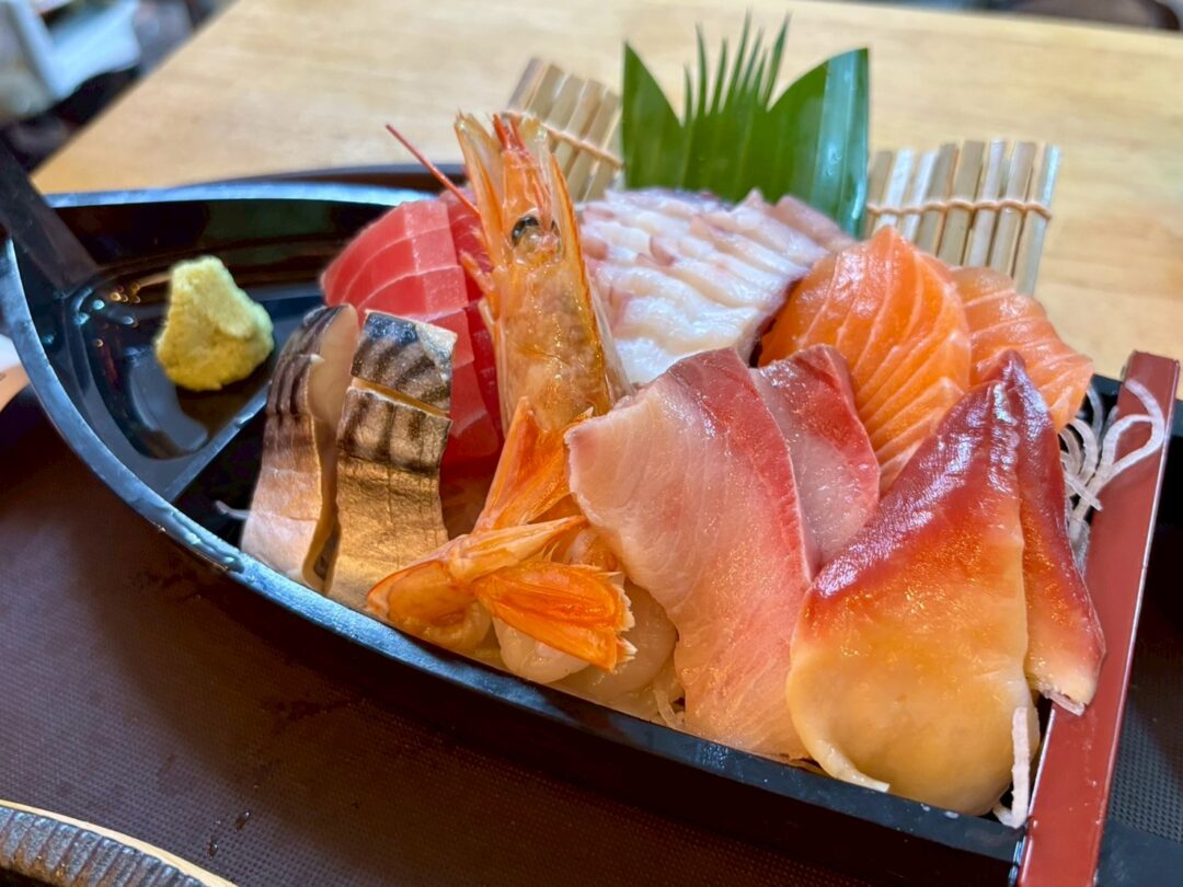 舟の器に美しく盛り付けられた、新鮮な刺身の盛り合わせ。マグロ、サーモン、エビ、イカなどが確認できる。