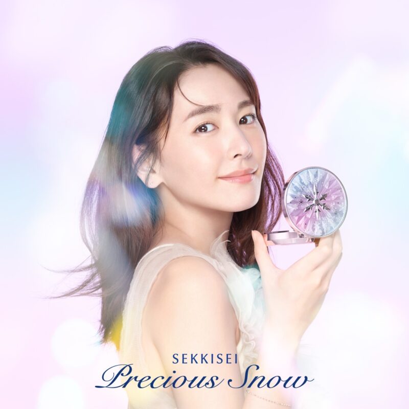 微笑む女性が「雪肌精 Precious Snow」のコンパクトを手に持ち、柔らかな光に包まれている。
