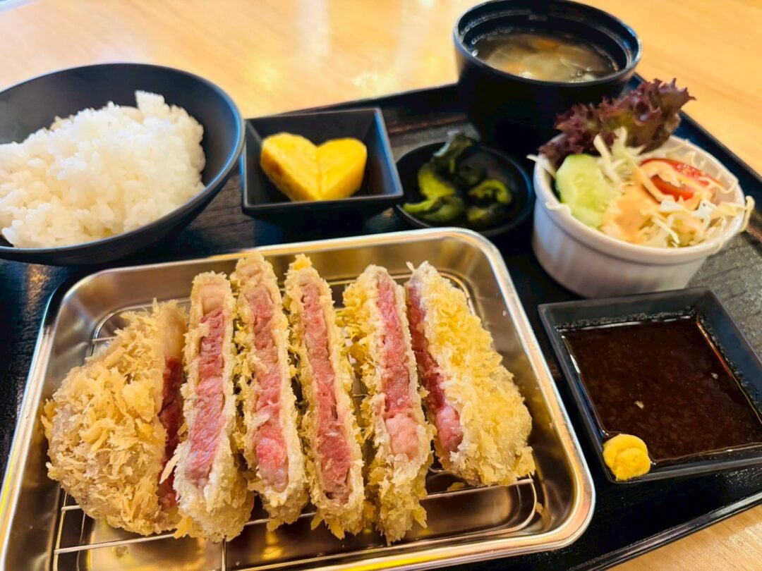 牛かつ定食。一口大に切られた牛かつと、ご飯、味噌汁、サラダ、漬物、卵焼きがトレーに載っている。