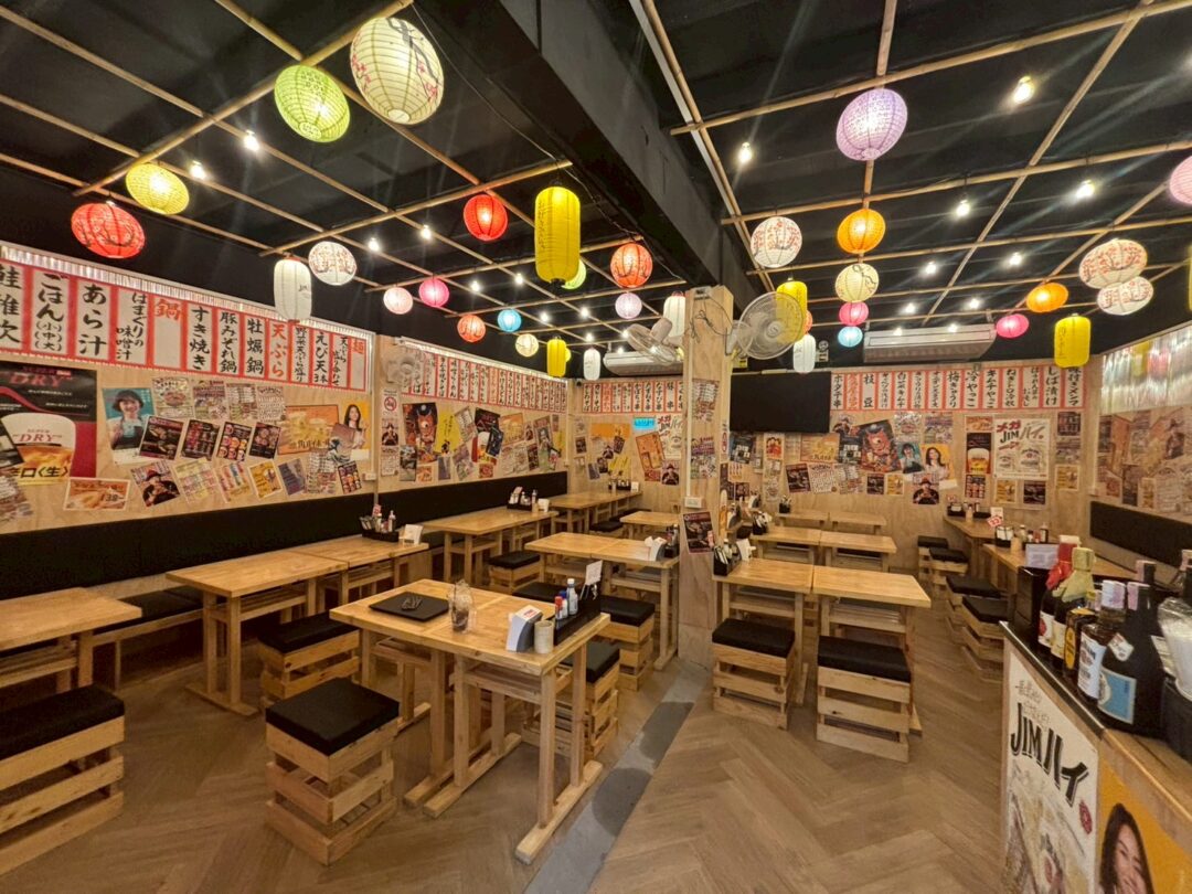 提灯が飾られた、居酒屋「恵美須商店」の活気ある店内。テーブル席が多数並び、壁にはポスターが貼られている。