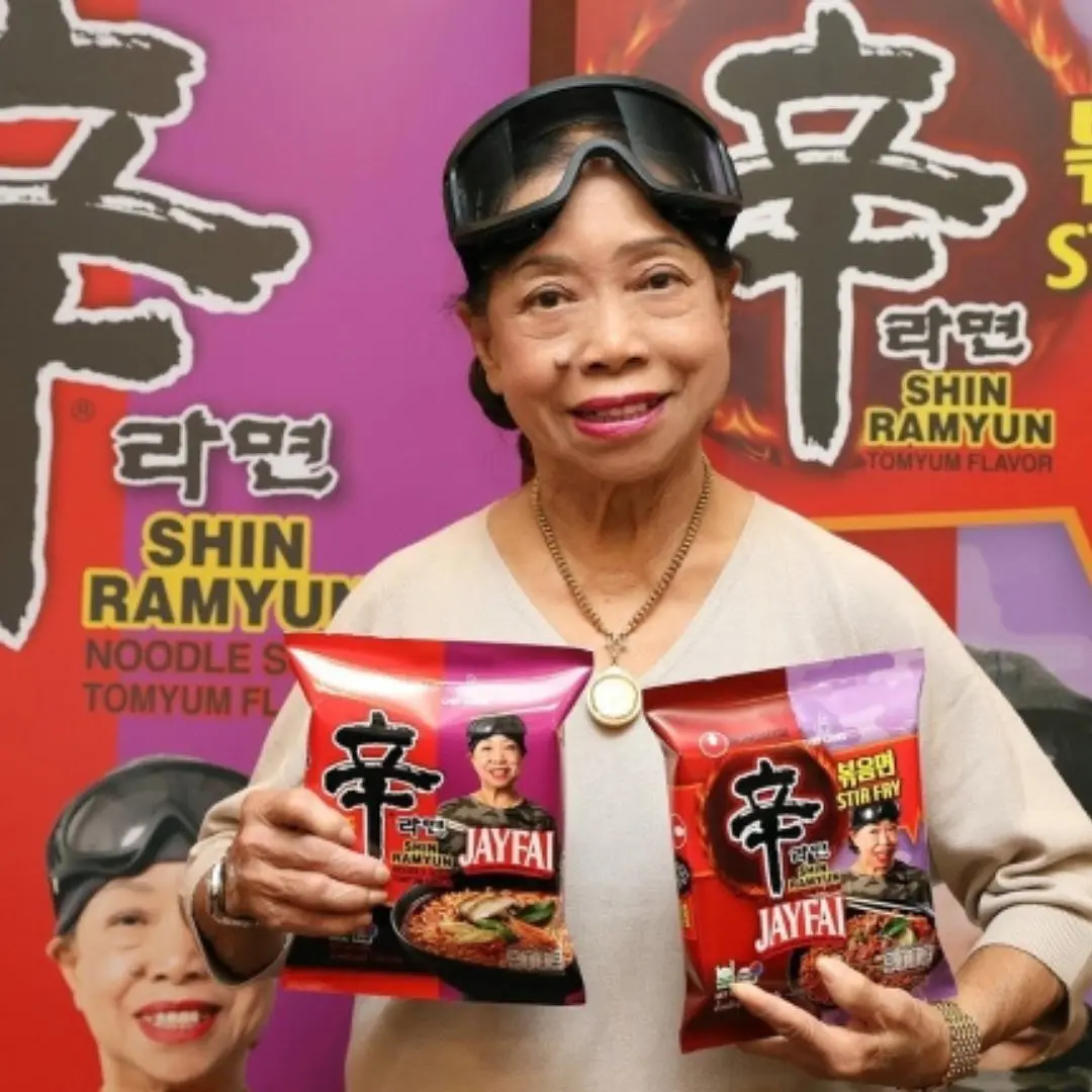 ジェイファイ(Jay Fai)が辛ラーメンとコラボしたパッケージを手に持つ姿。ミシュラン一つ星のストリートフードシェフとのコラボ即席麺。