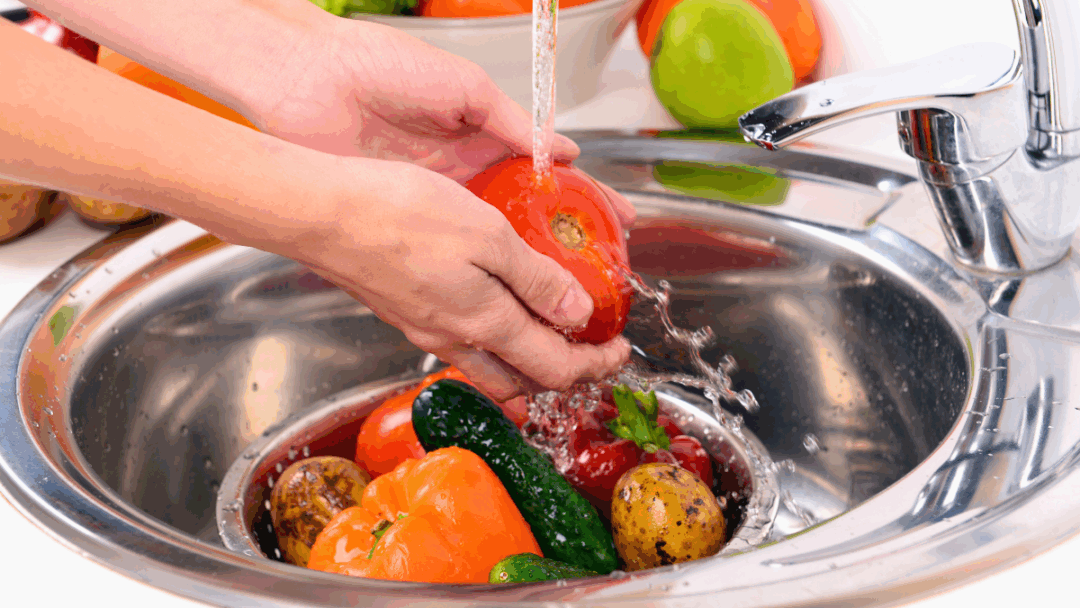 キッチンシンクでトマトを流水で洗っている様子。タイの野菜の残留農薬や寄生虫を落とすための基本的な洗浄方法を示す画像。
