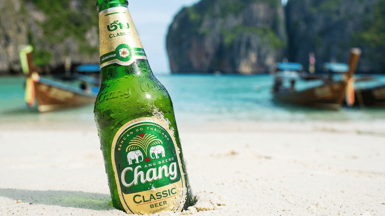 タイのチャンビール(Chang Beer)値上げニュースのサムネイル画像。タイのピピ島マヤベイを背景に、砂浜に置かれた瓶ビールの写真。